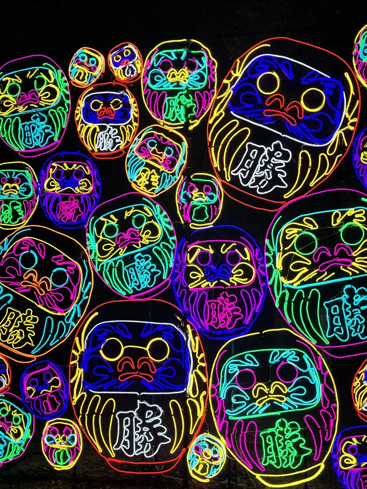 Muro de darumas dibujados en neón de colores sobre fondo negro, en Osaka